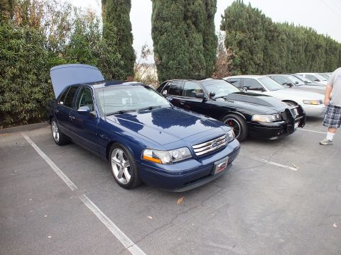 2003 Ford Crown Victoria - Dark blue Ford Crown Victoria with trunk open and chrome wheels next to a black push-bar Crown Victoria