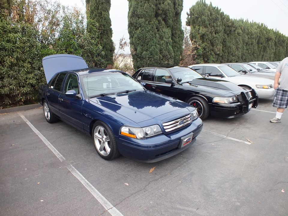 Blue Ford Crown Victoria with open trunk beside black push-bar sedan in lot