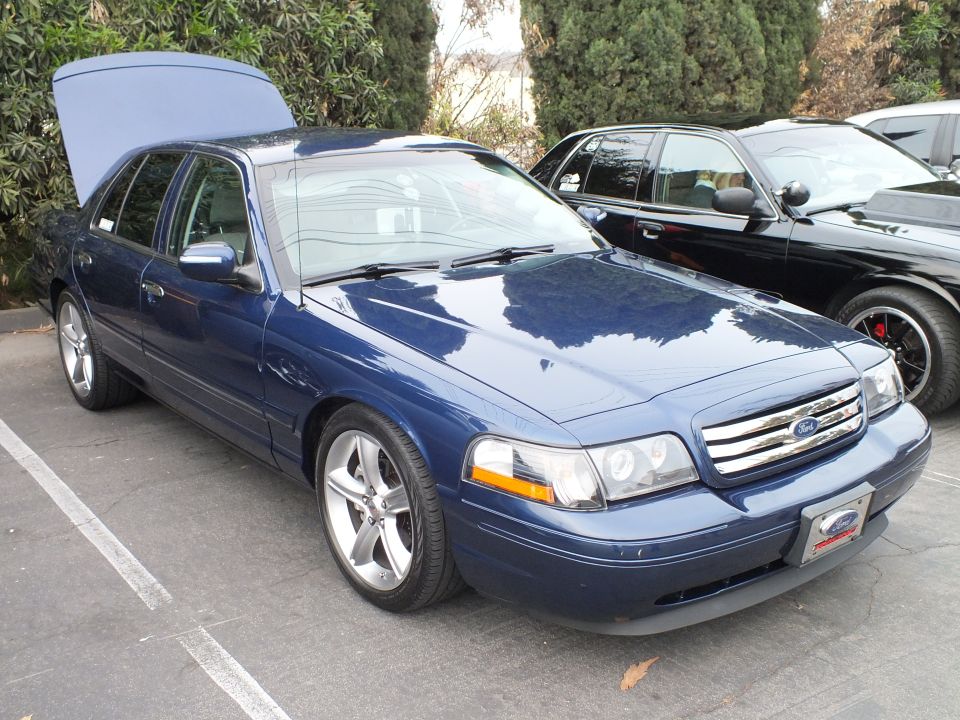 Blue Ford Crown Victoria with open trunk and projector headlights in parking lot