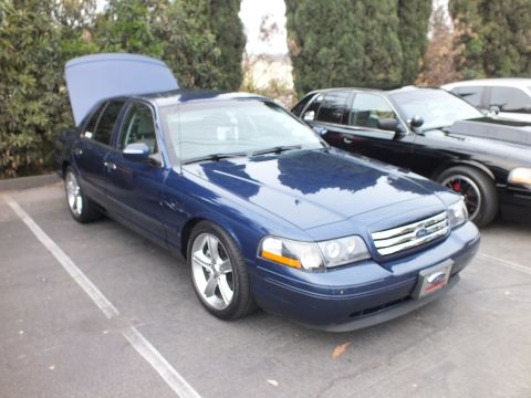 2003 Ford Crown Victoria - Blue Ford Crown Victoria with trunk open and chrome wheels next to a black sedan showing red brake calipers
