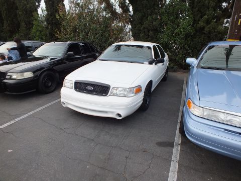 2003 Ford Crown Victoria - White Ford Crown Victoria parked between a black push-bar Crown Victoria and a light blue sedan