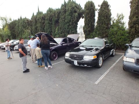 2003 Ford Crown Victoria - Black Ford Crown Victoria parked as a group of people gather around adjacent open-hood sedans