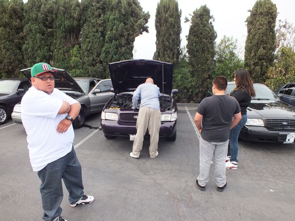 Ford Crown Victoria with hood up at parking lot car meet, people standing nearby