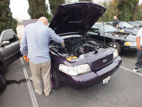 2003 Ford Crown Victoria - Man bends over the engine bay of a purple Ford Crown Victoria parked among other sedans.