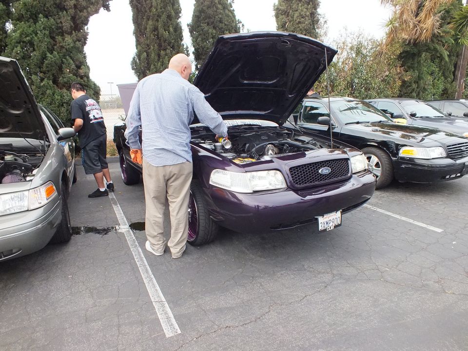 Purple Ford Crown Victoria with raised hood, people working on engines at outdoor meet