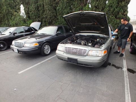2003 Ford Crown Victoria - Man in gloves works on a green Crown Victoria beside a black Crown Victoria at a car meet.