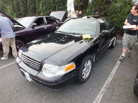 2003 Ford Crown Victoria - Black Ford Crown Victoria parked at a meet with a yellow cloth on the hood and people behind.
