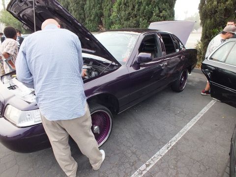 2003 Ford Crown Victoria - Side profile of a lowered purple Crown Victoria on wire wheels as a man works under the hood.