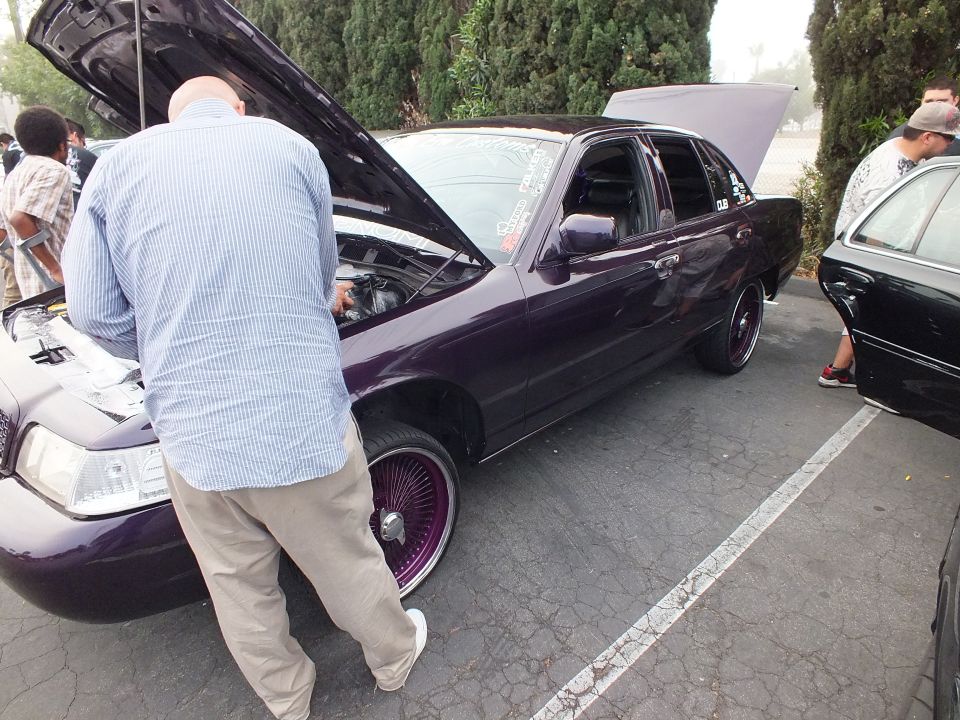 Purple Ford Crown Victoria side view, hood open, purple wire wheels, man working on engine