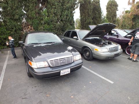 2003 Ford Crown Victoria - Gray Crown Victoria parked beside a green Crown Victoria with raised hood at a sedan gathering.