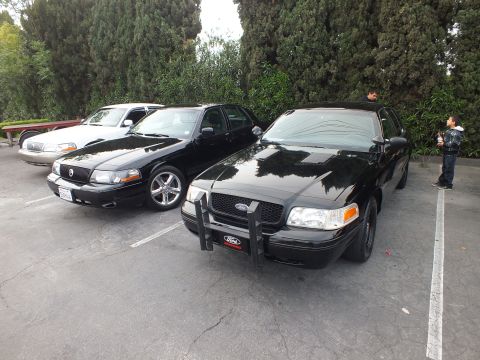 2003 Ford Crown Victoria - Black Mercury Grand Marquis beside a black Crown Victoria fitted with a push bar at a car meet.