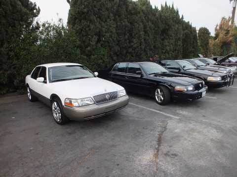 2003 Ford Crown Victoria - Two-tone white and tan Mercury Grand Marquis parked at the end of a row of black sedans.