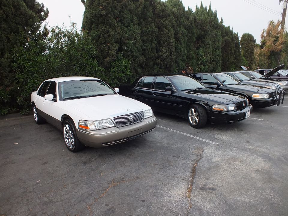 White and tan Mercury Grand Marquis parked beside black sedans at outdoor car meet