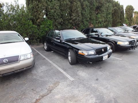 2003 Ford Crown Victoria - Black Mercury Marauder sits angled in a lot surrounded by Crown Victorias and a Grand Marquis.