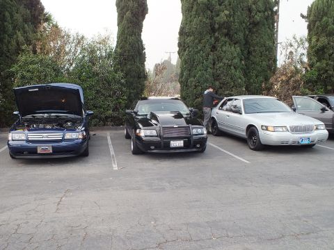 2003 Ford Crown Victoria - blue Ford sedan with hood raised, a black sedan with brush guard, and a silver Mercury Grand Marquis parked side by side.