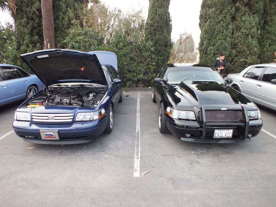 Blue Ford sedan with hood up beside black sedan with brush guard and EVIL VIC plate