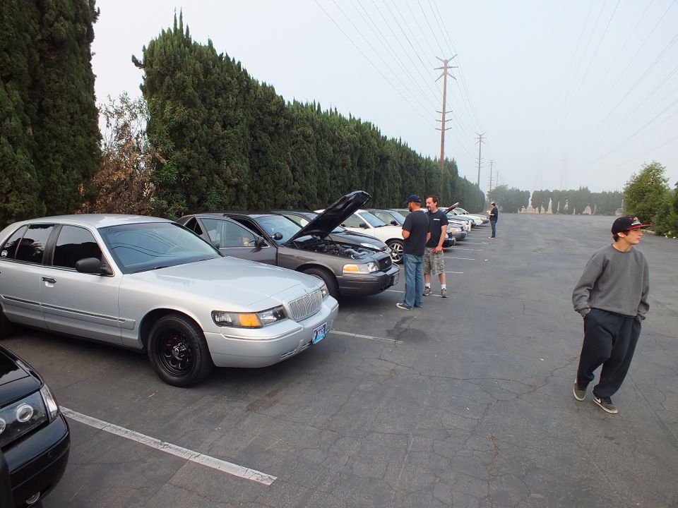 Silver Mercury Grand Marquis leading a row of parked sedans with people nearby