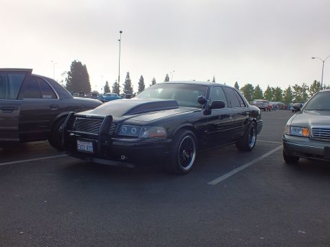2003 Ford Crown Victoria - lowered black full-size sedan with a brush guard and ram-air style hood parked at an angle in an open lot at dusk.