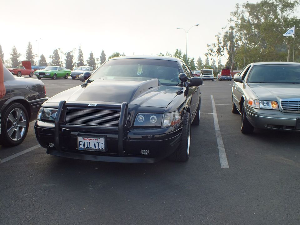 Front view of black sedan with push bar and EVIL VIC plate at a car show