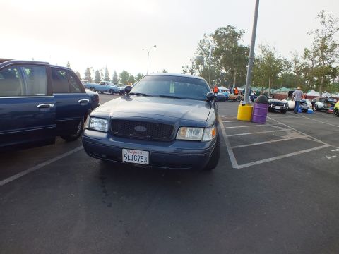 2003 Ford Crown Victoria - dark gray Ford full-size sedan photographed head-on, showing the oval grille badge and a California license plate at a car meet.