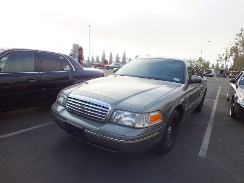 2003 Ford Crown Victoria - gray-green Ford full-size sedan shown in front three-quarter view with chrome grille and black steel wheels at a car meet.