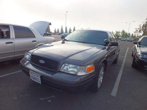 2003 Ford Crown Victoria - charcoal gray Ford full-size sedan in front three-quarter view with a California plate reading 6YWN854, parked among other cars.