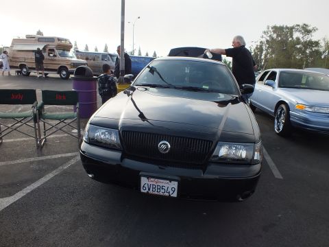 2003 Ford Crown Victoria - black Mercury full-size sedan seen from the front with the trunk open and a California plate 6VBB549, at an outdoor car meet.