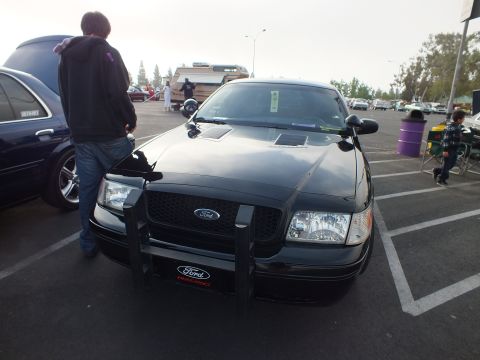 2003 Ford Crown Victoria - black Ford full-size sedan with a police-style push bar and Ford Performance plaque, parked at a car meet with people standing around.