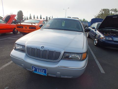 2003 Ford Crown Victoria - silver Mercury full-size sedan shown head-on with the waterfall grille badge and a Nevada plate reading RAGE, parked at a meet.