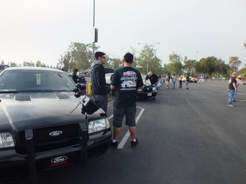 2003 Ford Crown Victoria - Two men in dark clothing stand beside a black full-size sedan with a push bar at an outdoor parking-lot car meet.