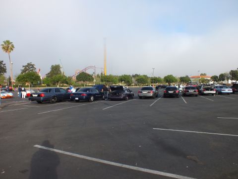 2003 Ford Crown Victoria - Several cars are parked in a large lot with a roller coaster visible on the horizon under a hazy morning sky.