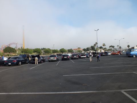2003 Ford Crown Victoria - wide parking lot holds rows of parked cars with people gathered nearby and a roller coaster on the hazy horizon.