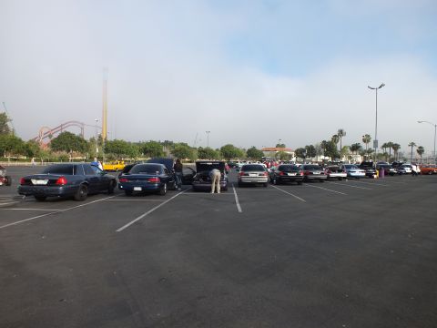 2003 Ford Crown Victoria - Several dark sedans sit in a hazy lot, one with its trunk open as a person reaches inside, a roller coaster faint in the background.