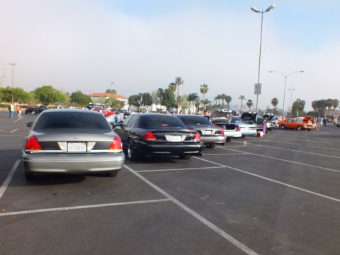 2003 Ford Crown Victoria - Silver and black full-size sedans seen from behind in a parking lot, with hoods raised on cars farther down the row.