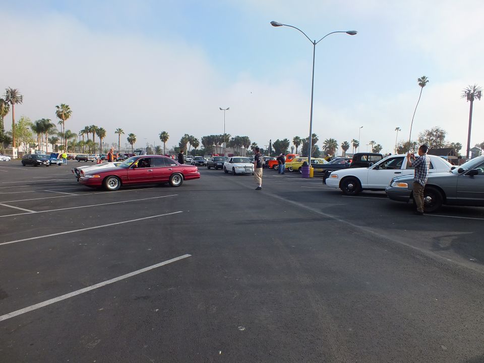 Red lowered sedan driving across a parking lot with a white sedan nearby