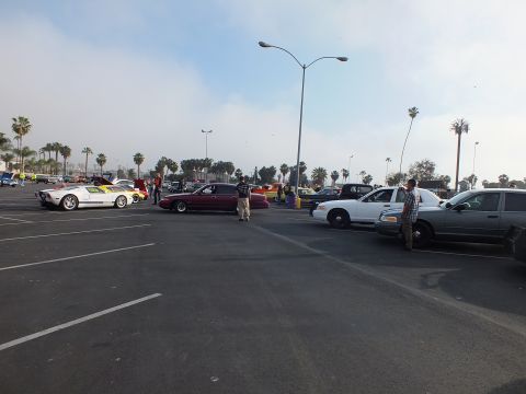 2003 Ford Crown Victoria - white mid-engine sports car and a maroon sedan sit among police-style sedans at a car meet, with people standing around.