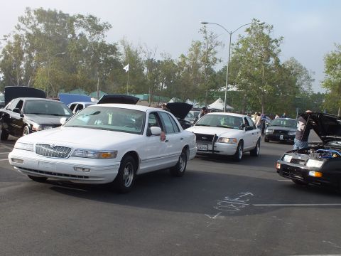 2003 Ford Crown Victoria - white Mercury full-size sedan faces the camera at a car meet, with white and black police-style sedans lined up behind it.