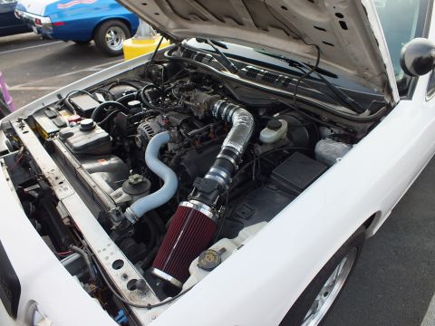 2003 Ford Crown Victoria - open engine bay showing a modified cold-air intake with a red cone filter and a silver charge pipe on a white car.