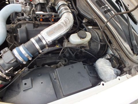 2003 Ford Crown Victoria - Close-up of an engine bay showing a heat-wrapped silver intake tube, blue couplers and the brake master-cylinder reservoir.