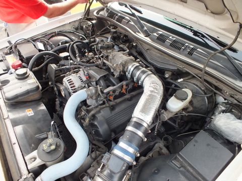 2003 Ford Crown Victoria - engine bay showing the alternator, a blue coolant hose and a silver heat-wrapped intake tube, with a person in red leaning over.