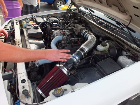 2003 Ford Crown Victoria - white car's engine bay with a red cone air filter and silver intake piping as a hand reaches in toward the components.