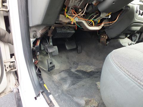 2003 Ford Crown Victoria - driver footwell of a car showing exposed colorful wiring above the pedals on worn gray carpet.