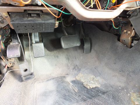 2003 Ford Crown Victoria - pedal box with three pedals and a relay/fuse panel above, surrounded by exposed wiring on gray floor matting.