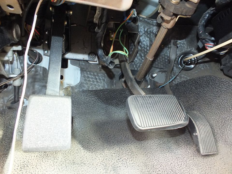 Three under-dash pedals with green and orange wiring on gray carpet