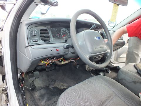 2003 Ford Crown Victoria - Driver-side interior of a sedan undergoing work, with the lower dash panel removed exposing colorful wiring and a Ford-badged steering whee…