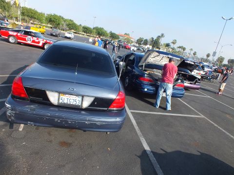 2003 Ford Crown Victoria - Rear of a dark blue Ford sedan displaying California plate 5LTG753, parked among other cars and people at an outdoor show.