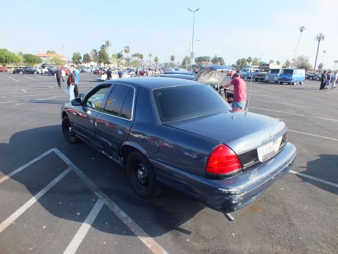 2003 Ford Crown Victoria - dark blue Ford sedan with black steel wheels shown from the rear three-quarter angle at a crowded outdoor car gathering.