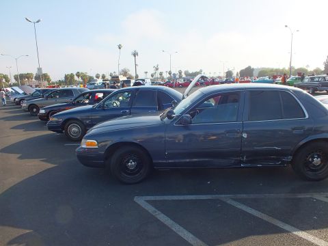 2003 Ford Crown Victoria - Several dark blue Ford sedans lined up in a parking lot, the nearest showing its side profile on black steel wheels.