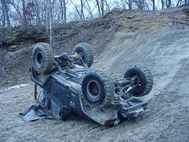 Mud-covered SUV flipped upside down on a steep dirt off-road trail