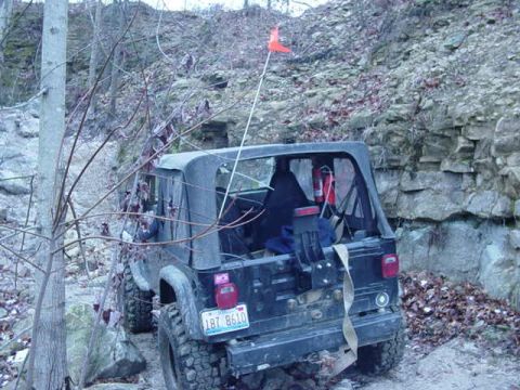 1992 Ford Bronco - Rear view of a Jeep Wrangler parked on a rocky, wooded trail. An orange flag is attached to the antenna.